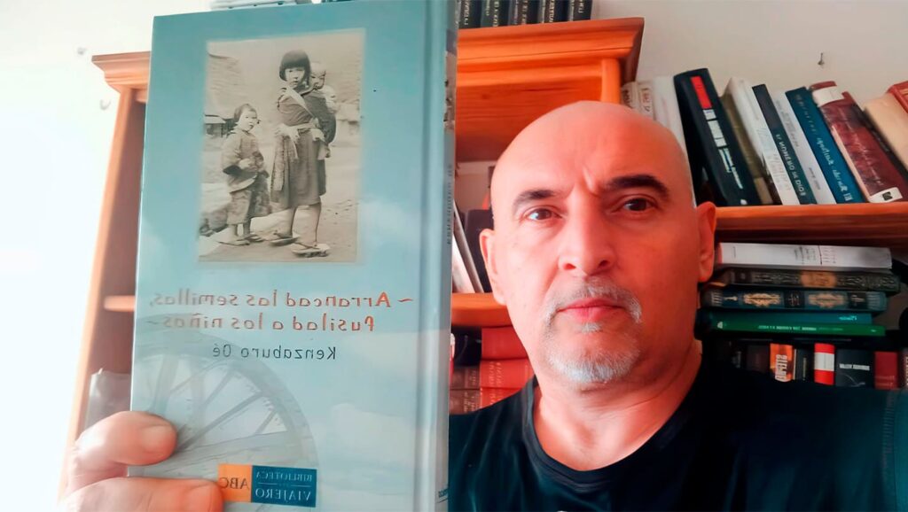 Gallego Rey sosteniendo un ejemplar de Arrancad las semillas, fusilad a los niños, la novela de Kenzaburō Ōe, como parte de la reseña crítica y análisis.